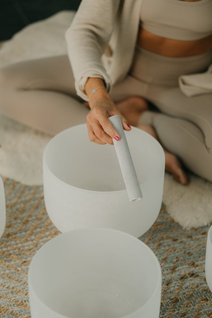 A woman in neutral tones playing a crystal singing bowl for meditation and relaxation.