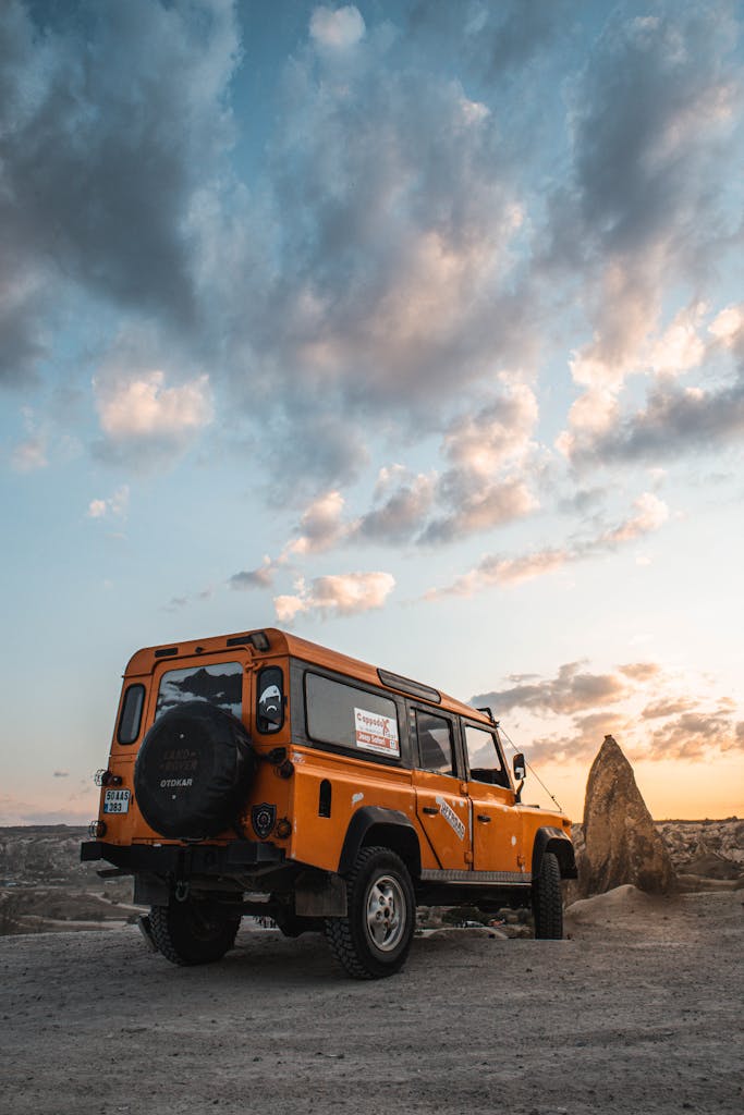 Explore rugged terrains with an orange off-road vehicle under a vibrant sunset sky.